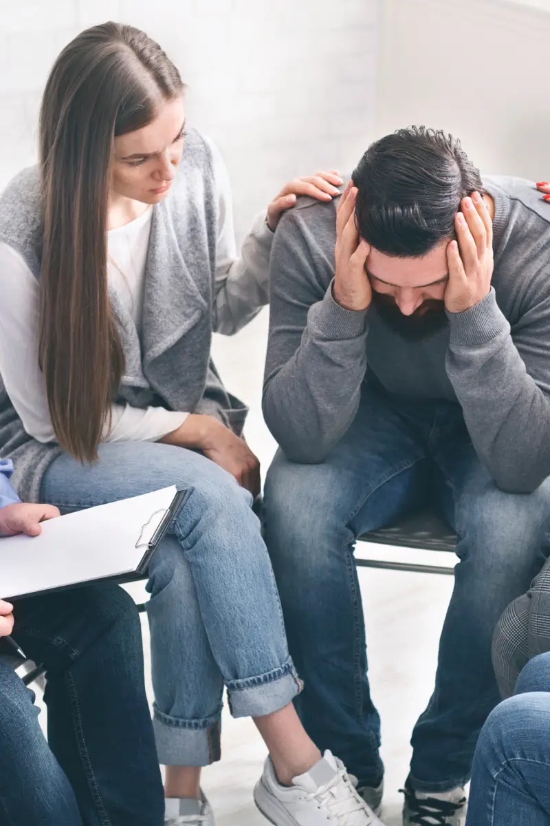 Depressed man with alcoholism problem sitting in rehab center, group supporting him, free space